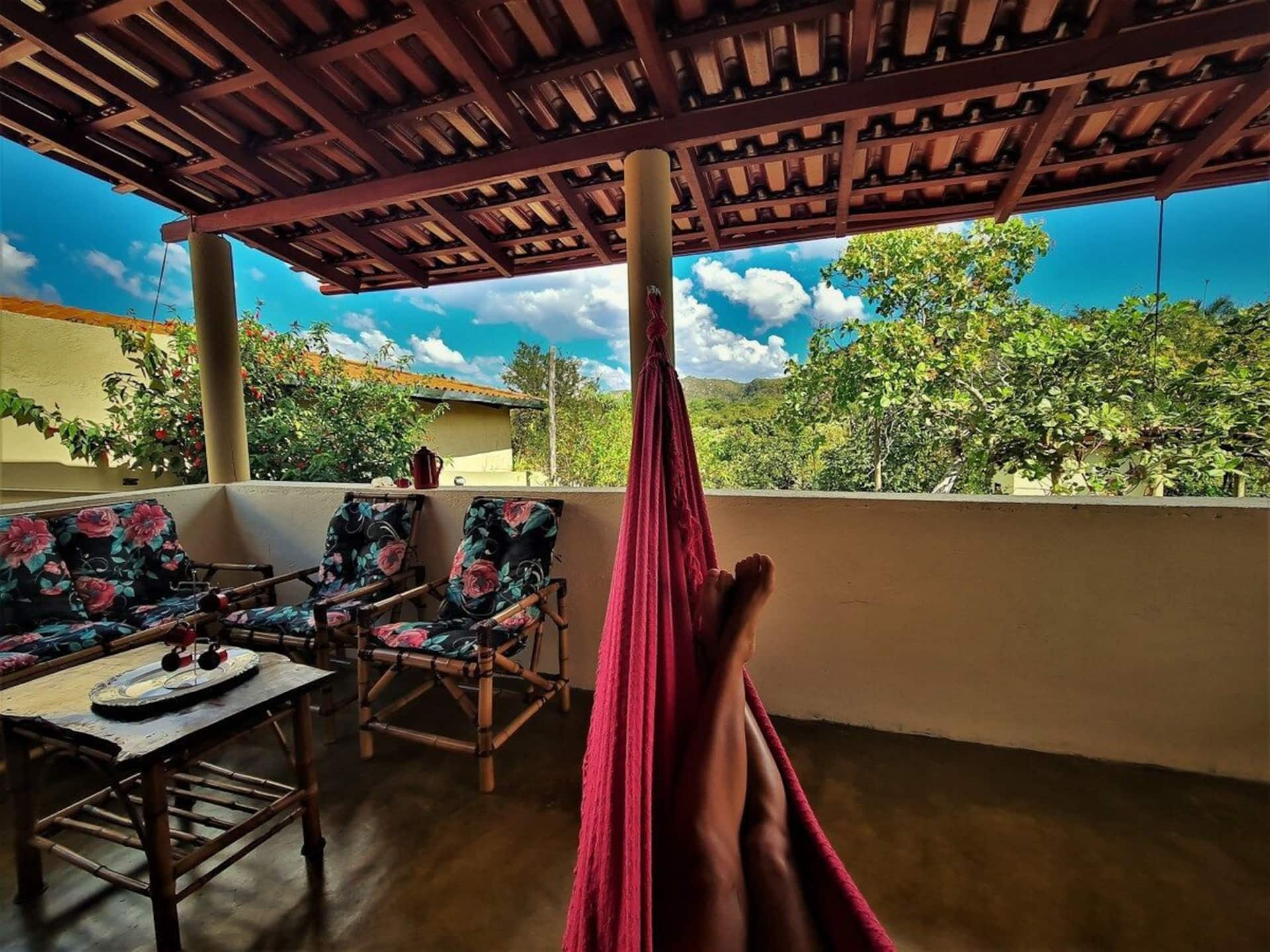 Varanda da Casa da Artista, com rede, mesa e vista para a serra